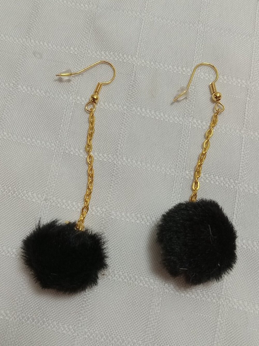 Handmade earrings with small pom-poms and gold-colored accent hooks and chains
